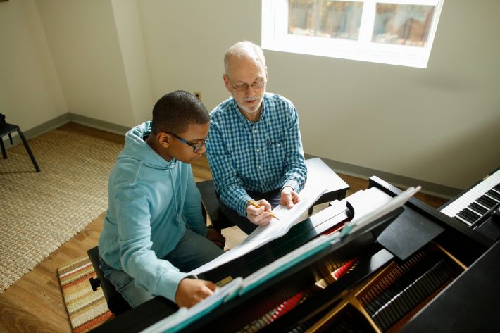 A Piano teacher points out something in a musical score.