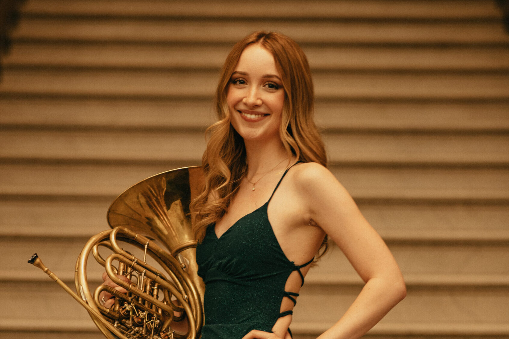 Photo of Lea Helsel ‘25, French Horn, holding their instrument on the steps of Lowry Hall