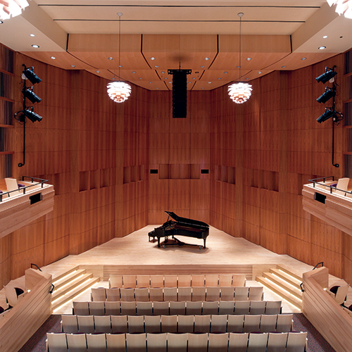A photo looking down at the stage of an empty Hatch Recital Hall from upper seats. A piano sits alone on the stage itself.