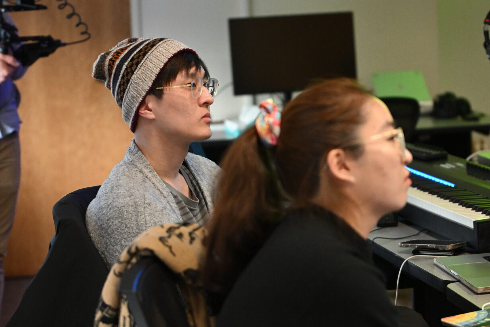 Two students sitting in a media lab setup, looking out of frame