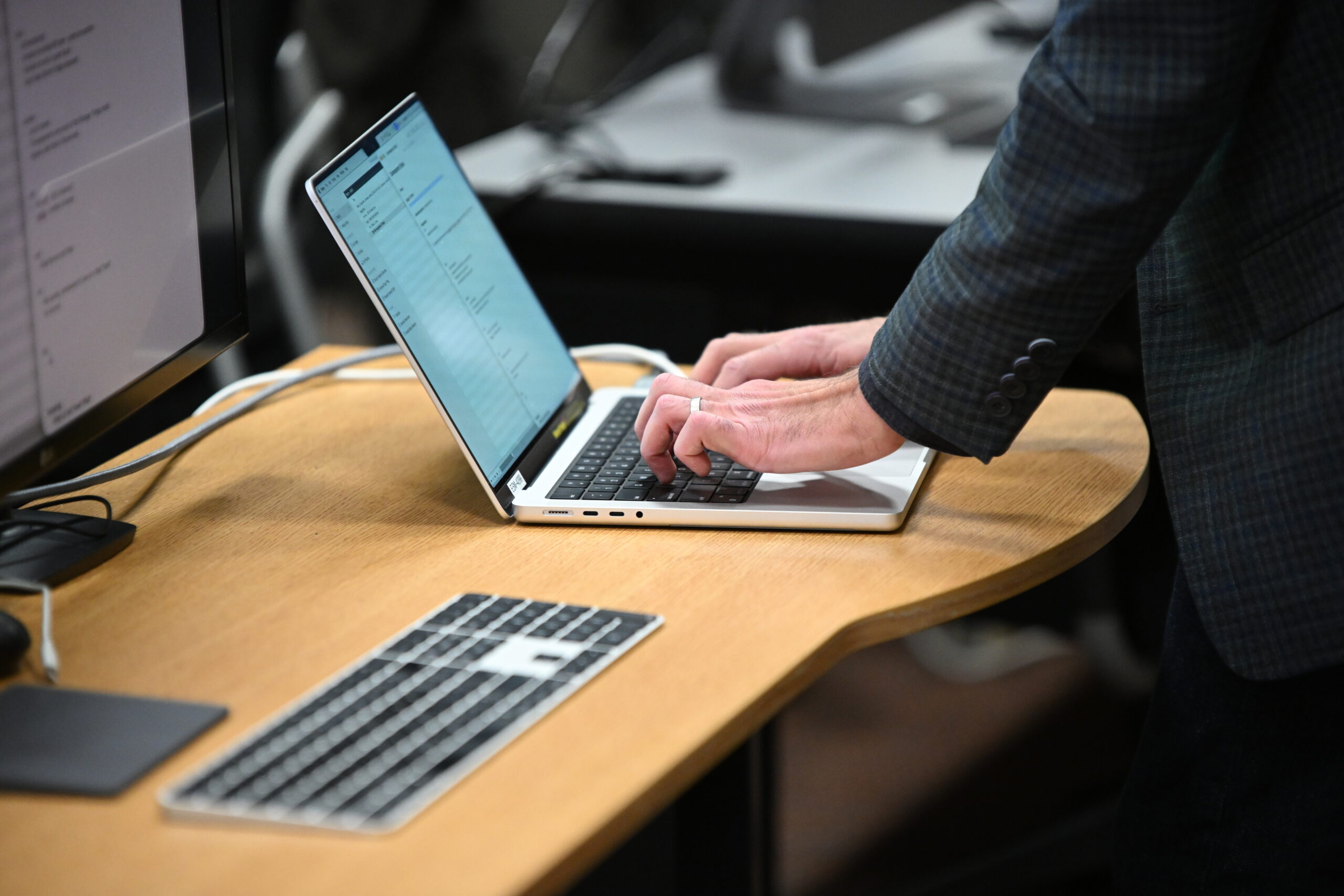 Hands typing on a laptop sitting on a media lab table with a keyboard and monitor nearby
