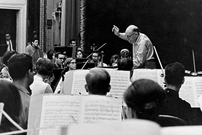 Igor Stravinsky conducts a student orchestra on the Eastman Theatre stage, viewed from the 3rd row of the 2nd violin section.