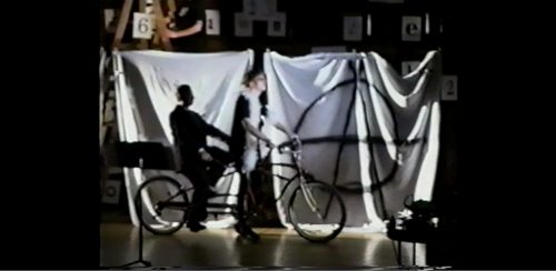 two performers re-entering the stage, this time together on a tandem bicycle