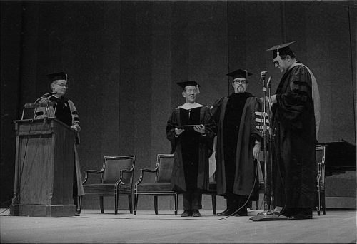 Conferral of an honorary doctoral degree on Shinichi Suzuki. Professor Donald Shetler hoods the newly named Dr. Suzuki; University President Robert Sproull stands at far left, and ESM Director Walter Hendl stands at far right.
