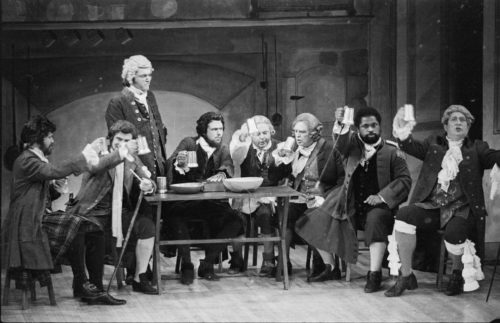 R2250-16A In the tavern in act I. The eight men on-stage are Parchment (standing), Raccoon (second from right), Washball (far right), and the rest, in no particular order, are Jack Rattletrap, Quadrant, Hum, Trushoop, and McSnip. Parchment, Hum, Quadrant, and Rattletrap are the four so-called Humorists who devise a cunning trap b which to exploit others for gain.