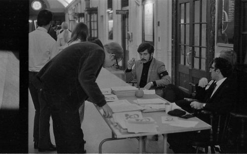 An information center set up in the main hall. The young man at center (seated) is wearing the black armband that was one of the symbols promoted on the day of the Moratorium.