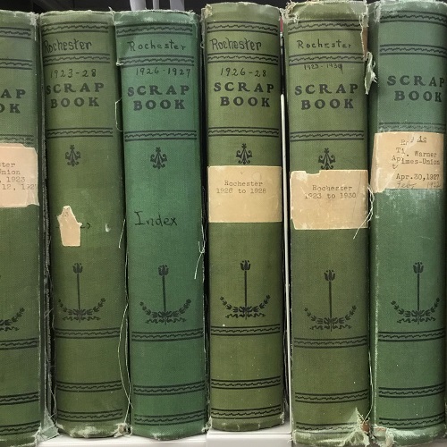 The spines of six green, cloth-bound scrapbooks dating from the 1920s filed on a shelf.