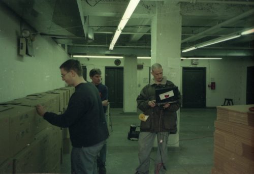 team members Brodsky, Coppen and Quinn are seen among the lines of shipping crates