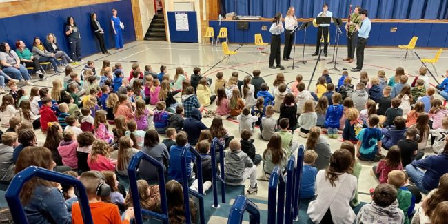 Children listening to chamber music group in school gymnasium