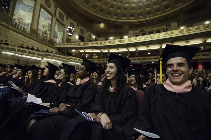 A row of smiling students in graduation caps and gowns in the theater. 