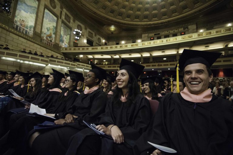 A row of smiling students in graduation caps and gowns in the theater.
