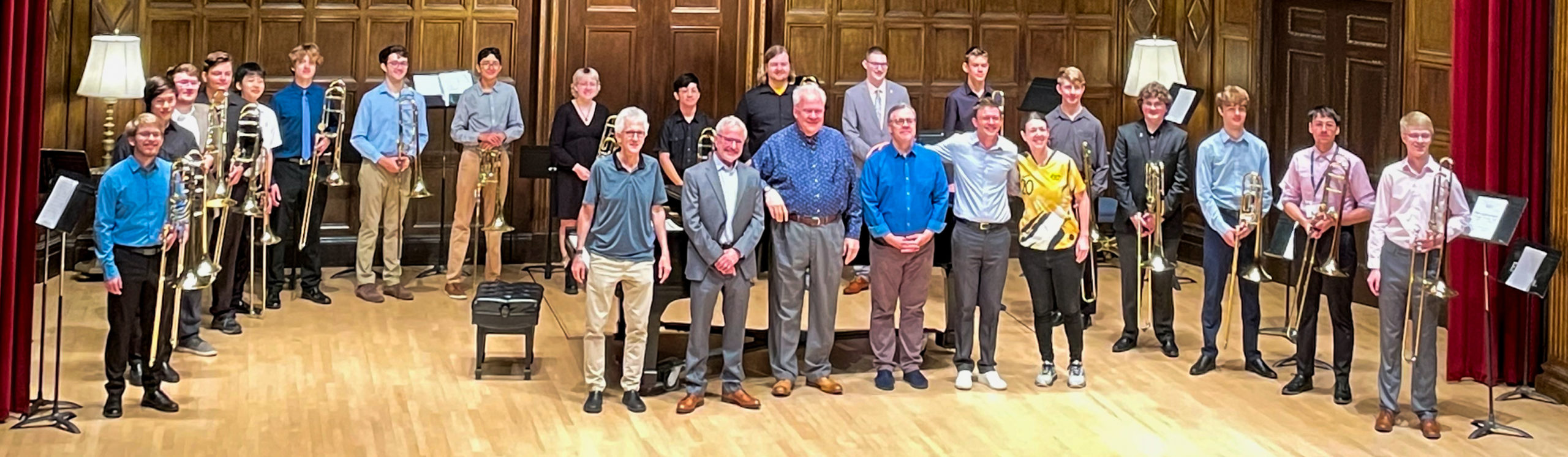 A large group of trombone players stand in a semi-circle on stage in Kilbourn Hall during Summer at Eastman 2023