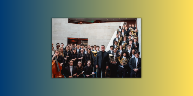 Eastman Wind Orchestra students stand with conductor Mark Scatterday in Lowry Hall at Eastman School of Music