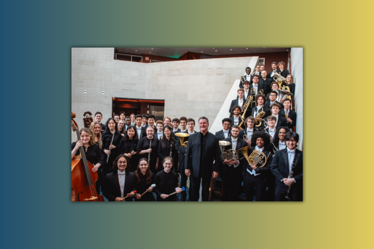 Eastman Wind Orchestra students stand with conductor Mark Scatterday in Lowry Hall at Eastman School of Music