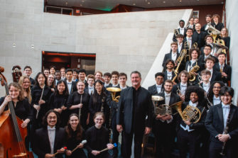 Eastman Wind Orchestra students stand with conductor Mark Scatterday in Wolk Atrium at Eastman School of Music