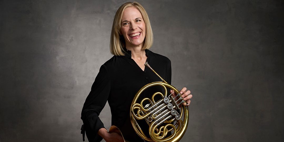 woman in black shirt, holding french horn.