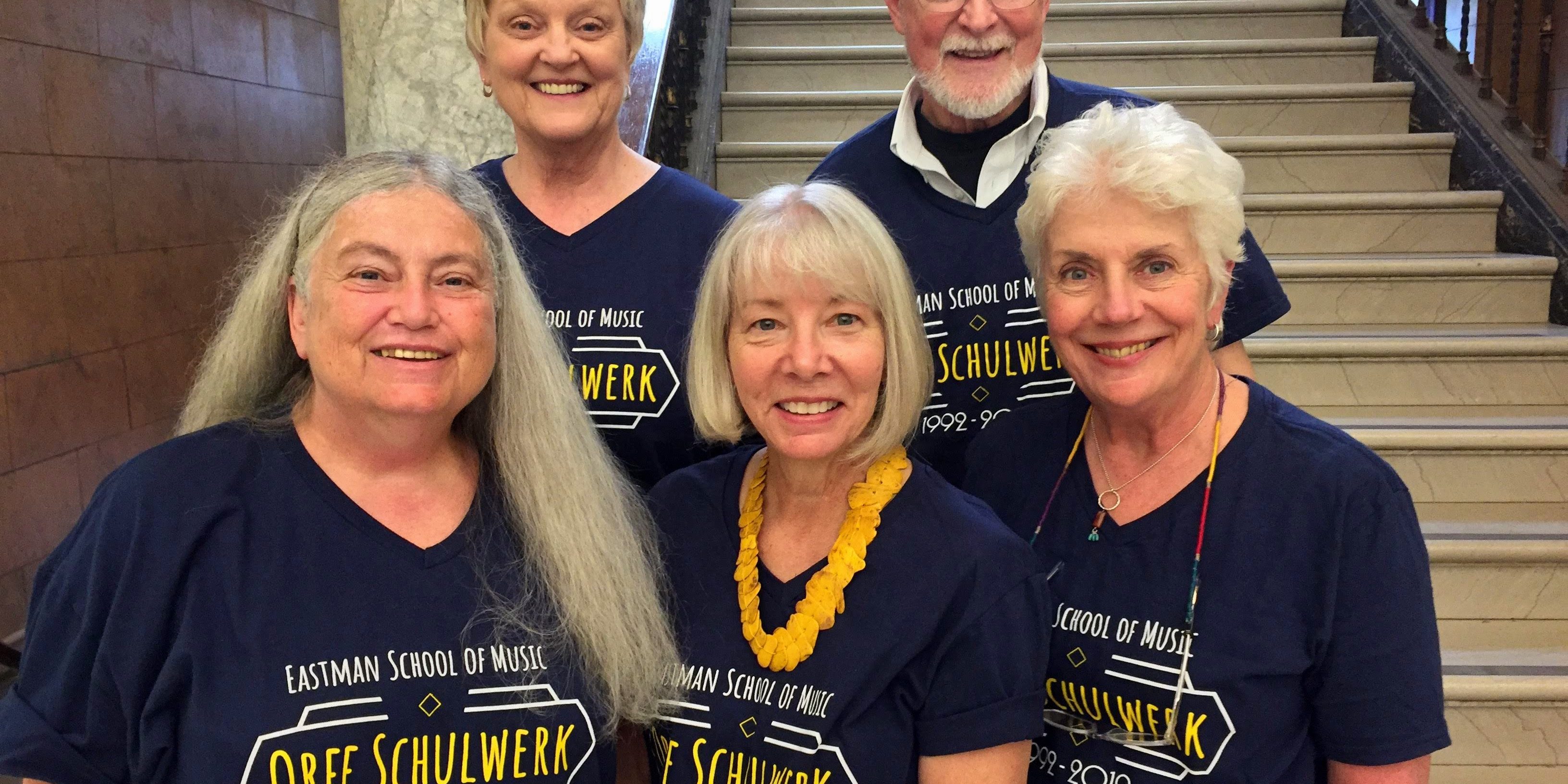 Five faculty members in dark blue T-shirts standing on staircase in Lowry Hall.