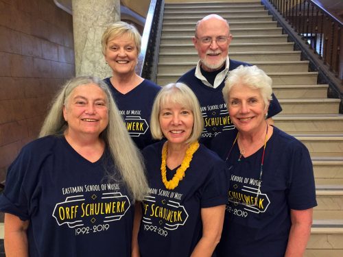 Five faculty members in dark blue T-shirts standing on staircase in Lowry Hall.