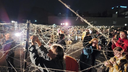 People in outdoor nighttime setting surrounded by art installation of string