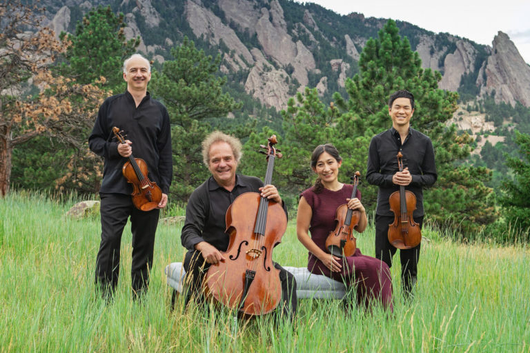 Takacs Quartet posed in a field with instruments, mountains in background